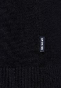 Pull noir en tricot avec un ourlet côtelé et une petite étiquette en tissu portant la marque "Jack & Jones" sur le côté. Texture douce et design classique.