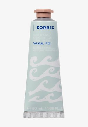 Crema per le mani Korres in un morbido tubetto menta, con motivi a onde bianche. Ha un tappo rosa e un testo che indica la fragranza "Fico Costiero".