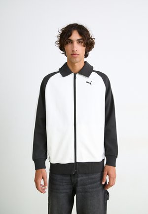 Puma zip-jakke med hvid krop og sorte ærmer, ribbede manchetter og en hævet krave. Logo på venstre bryst, blødt tekstureret stof.