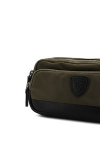 Pochette in nylon verde oliva con base in pelle nera, caratterizzata da una superficie testurizzata e un'etichetta con logo. Due scomparti con zip visibili.