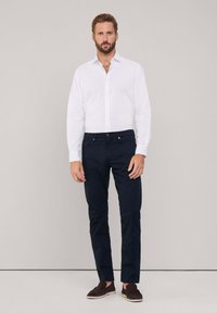 Witte button-up shirt, marineblauwe broek en bruine instapschoenen. Slim fit, gladde stof en minimalistisch ontwerp met een nette afwerking.