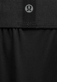 Fekete szövet, fodros varrással egy bordázott szalag alatt, középen elhelyezett, kis, kerek Lululemon logóval a szalagon.