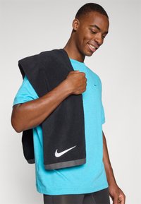 Sinine sportlik T-särk peene logoga, hoides musta rätikut halli äärise ja valge Nike brändinguga. Sujuv tekstuur, vabaja disain.