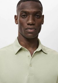 Ljusgrön polotröja med klassisk krage, tre knappar och en strukturerad väv. Närbild på tröjans halsringning och axlar.