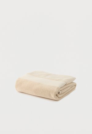 Serviette en tissu éponge pliée de couleur beige et blanc cassé, posée sur une surface blanche unie.