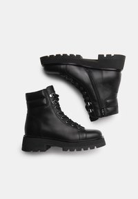 Black leather ankle boots with lace-up front, side zipper, and a chunky, textured sole. Features metal hardware and smooth finish.