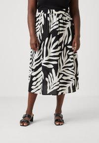 Jupe mi-longue noir et blanc avec un motif de feuilles, taille élastique et tissu léger. Portée avec des sandales à talons noires.