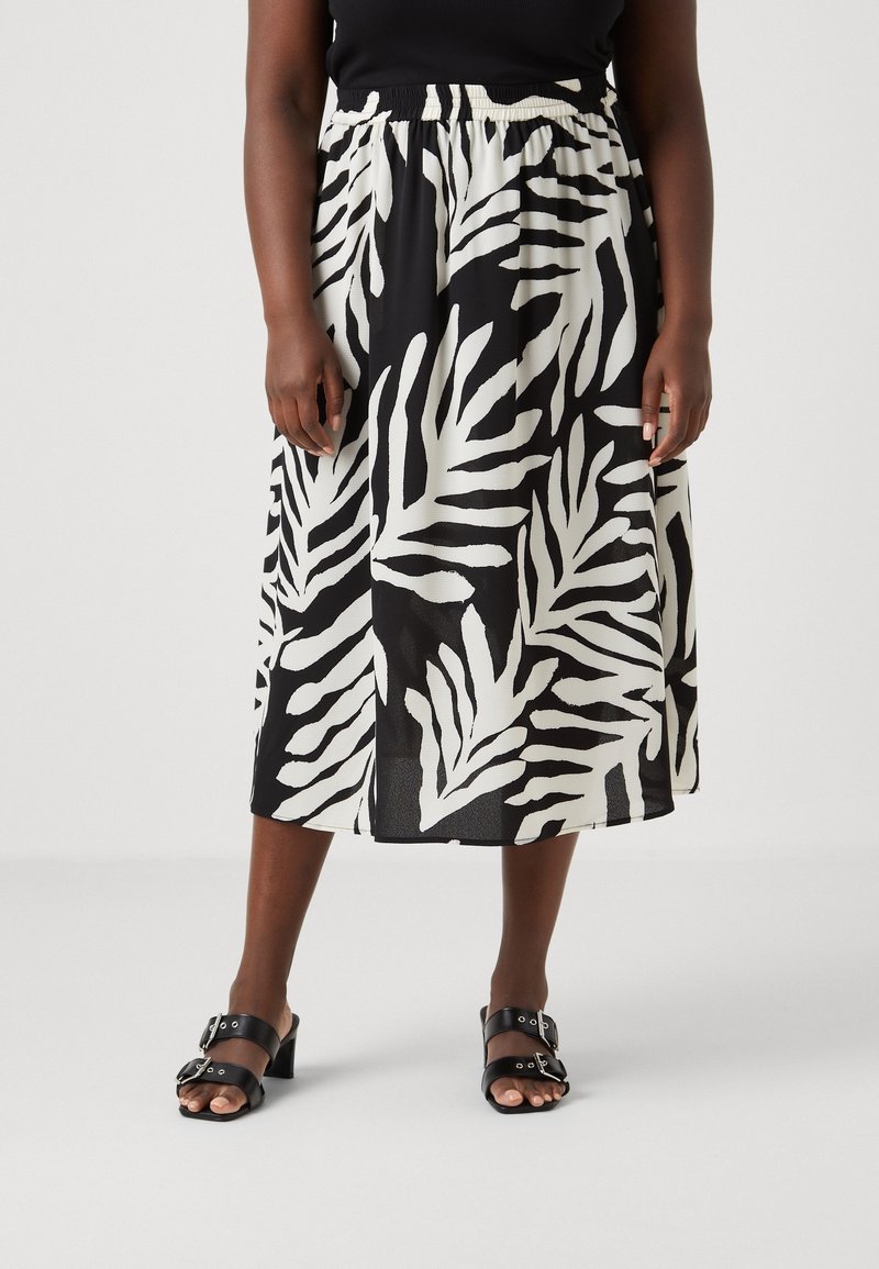 Jupe mi-longue noir et blanc avec un motif de feuilles, taille élastique et tissu léger. Portée avec des sandales à talons noires.