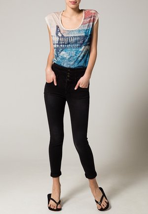 Kortærmet, multicolor grafisk T-shirt med tekst, parret med højtaljede sorte skinny jeans og sorte flip-flops.