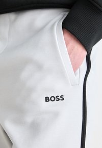 Light gray joggers with black accents, featuring a side pocket and "BOSS" logo in black text, made from soft, smooth material.
