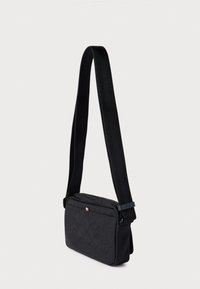 Fekete válltáska texturált anyagból, cipzáras tetővel, állítható pánttal és finom logó díszítéssel a pánton.