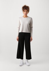 Lys beige langermet topp med rund hals, sammen med svarte vide bukser. Hvite høy-topp sneakers fullfører antrekket.