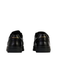 Sneaker in pelle nera con una finitura liscia, punta arrotondata e suola in gomma, con la scritta "REDSKINS" impressa in oro sul tallone.