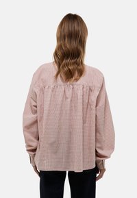 Chemise oversize à carreaux rouge et blanc avec un dos froncé, des manches longues et une coupe décontractée. Tissu léger, design décontracté.