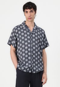 Camicia a maniche corte in tessuto blu scuro con un motivo geometrico bianco, dotata di colletto e chiusura con bottoni. Texture liscia e vestibilità comoda.