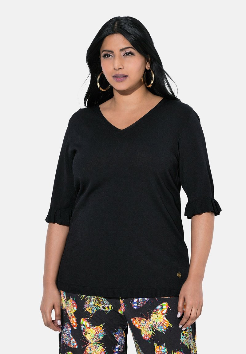Top nero a maniche corte con scollatura a V e maniche con volant, realizzato in tessuto liscio. Indossato con pantaloni colorati a fantasia farfalla.