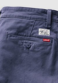 Gros plan de la poche arrière bleu marine d’un pantalon Levi's avec bouton, passants de ceinture et étiquettes en tissu et de marque Levi's.