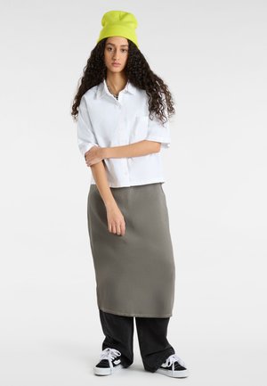 Camisa blanca de botones, falda maxi gris, pantalones anchos negros y zapatillas negras con cordones blancos, rematado con un gorro verde brillante.