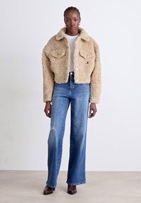 Beige kunstpels kort jakke med to frontlommer, kombinert med lyseblå høyt liv jeans med slitte detaljer.