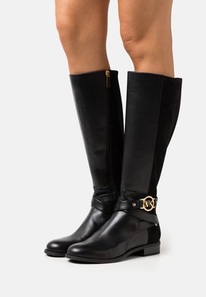 Bottes noires montantes en cuir lisse avec une fermeture éclair latérale, un talon bloc et un ornement décoratif doré à la cheville.