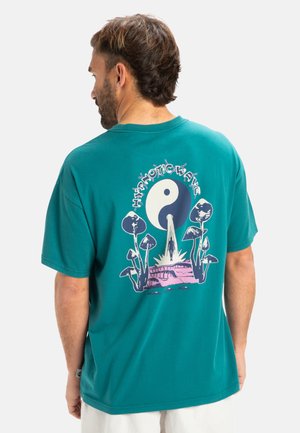Camiseta de algodón en color teal con un diseño gráfico en la parte trasera que presenta setas, un símbolo del yin-yang y el texto "Hypnotic Wave" en blanco y rosa.