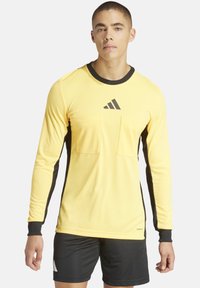 Gelbes langärmliges Sportshirt mit schwarzem Kragen und seitlichen Einsätzen, ausgestattet mit zwei Fronttaschen und einem Adidas-Logo auf der Brust.