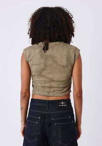 Top corto verde oliva con mangas cortas, que presenta una textura suave. Combinado con pantalones de mezclilla oscuros visibles en la cintura, que muestran bolsillos traseros.
