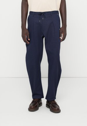 Pantalone u tamnoplavoj boji, lagani, izrađeni od mekanog materijala, s pojasom na vezivanje, nabranim prednjim dijelom i bočnim džepovima. Prikladni za svakodnevno nošenje.