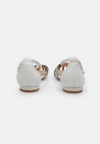 Chaussures en daim, à l'arrière fermé, de couleur gris clair avec des accents métalliques. Elles présentent un petit talon et un design ouvert avec des brides ajustables.