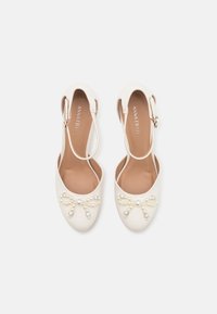 Weiße Slingback-Schuhe mit abgerundetem Zehenbereich, verziert mit einer Perlen- und Strassschleife an der Vorderseite. Glatte, glänzende Oberfläche.