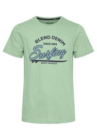 Světle zelené bavlněné tričko s kulatým výstřihem a krátkými rukávy. Grafika textu v tmavě modré a černé barvě: "BLEND DENIM Surfing BUILT IN BLUE."