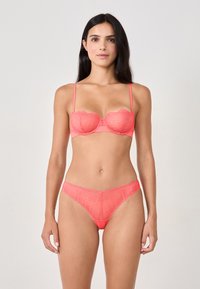 Set di lingerie in pizzo color corallo con reggiseno strutturato con ferretto e bordi smerlati decorativi, abbinato a un perizoma con rifinitura in pizzo.