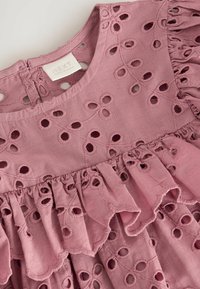 Rosa Baumwollbluse mit gestickten Blumenmustern, runden Ausschnitten, rüschgesäumtem Saum und Schlüssel-Loch-Verschluss auf der Rückseite. Markenlabel sichtbar.