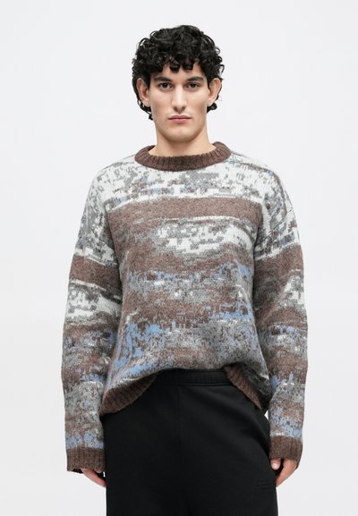 Pleteni pulover z teksturiranim vzorcem v rjavi, sivi, modri in beli barvi. Krožni izrez in široki rokavi z rebrastimi manšetami.