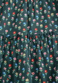 Kwiatowa sukienka w ciemnozielonym materiale z małymi, kolorowymi kwiatami w odcieniach czerwieni, różu, niebieskiego i żółtego, z falbaną u dołu i teksturowanymi plisami.