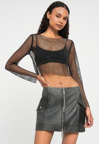 Svart mesh langermet topp over en svart crop top, paret med en grå faux skinn mini skjørt med glidelås foran og sidelommer.