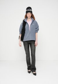 Ζακέτα με φερμουάρ από φλις σε ανοιχτό μπλε, συνδυασμένη με ροζ πουκάμισο, γκρι παντελόνι και μαύρα αξεσουάρ, περιλαμβανομένου ενός χνουδωτού κασκόλ και σκουφί.