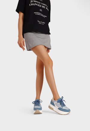 Sneaker blu e bianchi con tomaia in mesh e tessuto, punta rotonda, suola spessa e lacci a contrasto. Indossate con una maglietta nera con grafica e una gonna grigia.