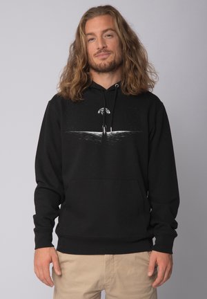 Black hoodie with a front pocket, featuring a white graphic design of a figure beside a tree and water, made from soft cotton material.