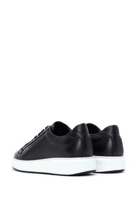 Sneakers in pelle nera con design a basso profilo, suola bianca e superficie liscia, con cuciture tonali e chiusura con lacci.