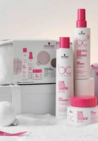 Tre hårvårdsprodukter i rosa och vit förpackning: schampo, spraybalsam och behandling. I sällskap av en vit kosmetikväska.