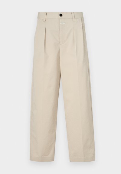 Beige wijde broek van katoen met voorplooien. Heeft een zwarte knoop en een label in de taille. Gladde textuur en op maat gemaakt ontwerp.