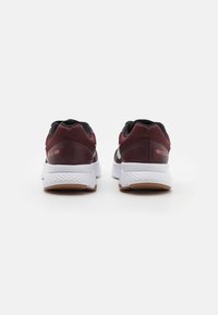 Baskets de sport maroon avec des accents en mesh noir, semelles blanches et semelles extérieures en caoutchouc texturé. Comprend un talon à motif et un détail de logo.
