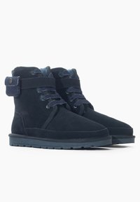 Botas de tobillo de ante en color azul marino con un collar acolchado, cierre de cordones y suela de goma texturizada. Incluyen una correa lateral con un detalle de logo.
