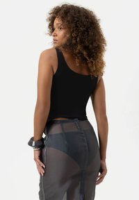 Zwart aansluitend tanktop gecombineerd met een semi-doorzichtige grijze rok met een zijsplit, waardoor de gelaagde texturen en het strakke ontwerp benadrukt worden.