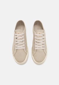 Baskets en toile beige avec bouts arrondis, design à lacets et semelles en caoutchouc texturées. Branding minimaliste sur la languette pour plus de détails.