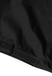Tissu noir avec une texture lisse, présentant une fermeture Velcro sur un bord, faisant partie d'un produit plus grand, avec peu de coutures ou d'ornements.