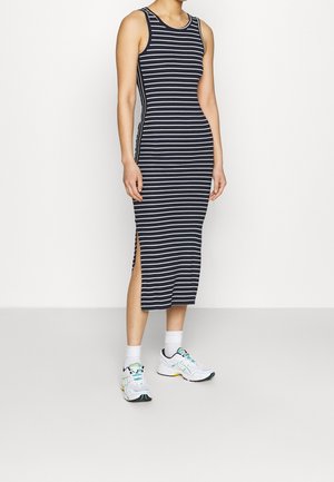 Ärmelloses marineblaues Midikleid mit weißen horizontalen Streifen und seitlichem Schlitz, getragen mit weißen Socken und weißen Laufschuhen.