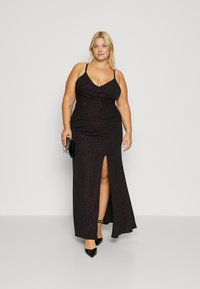Black, sparkly maxi dress with a V-neck, thin straps, draped detailing, and a thigh-high slit. Paired with a small black clutch and heels.