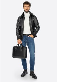 Zwarte leren bomberjack met een bontkraag, witte coltrui, blauwe spijkerbroek en zwarte leren laarzen; houdt een zwarte leren aktetas vast.